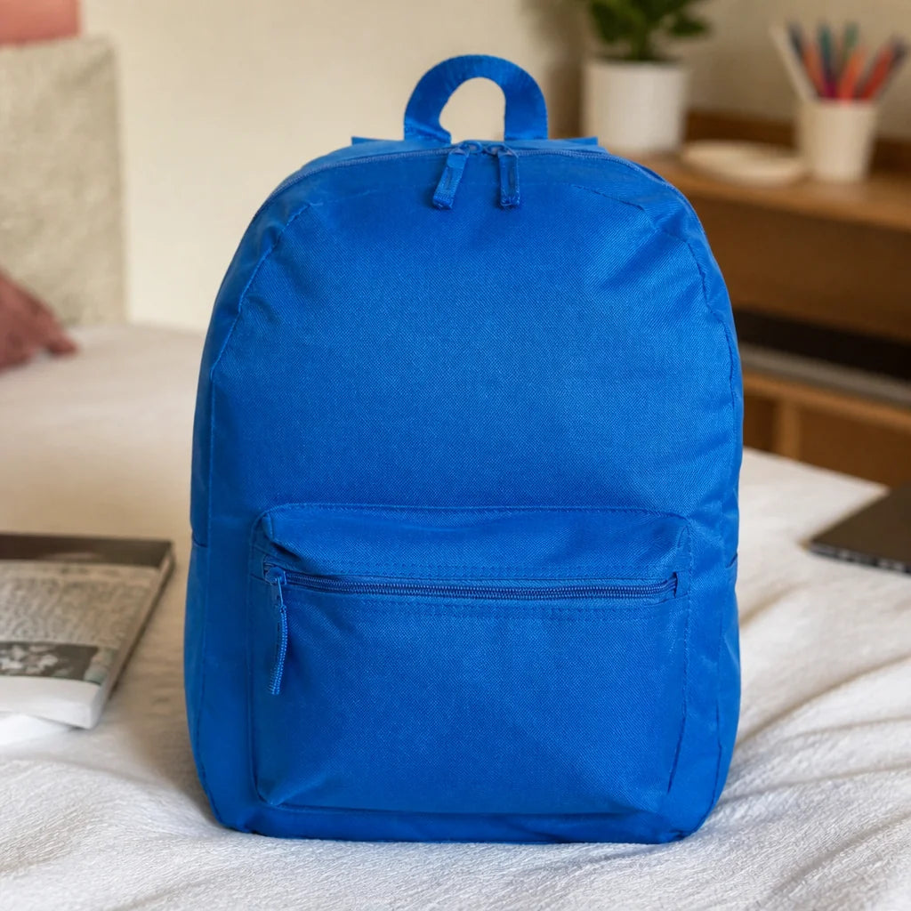 Customizable backpack in blue with a top handle and front zip pocket, on a white bed