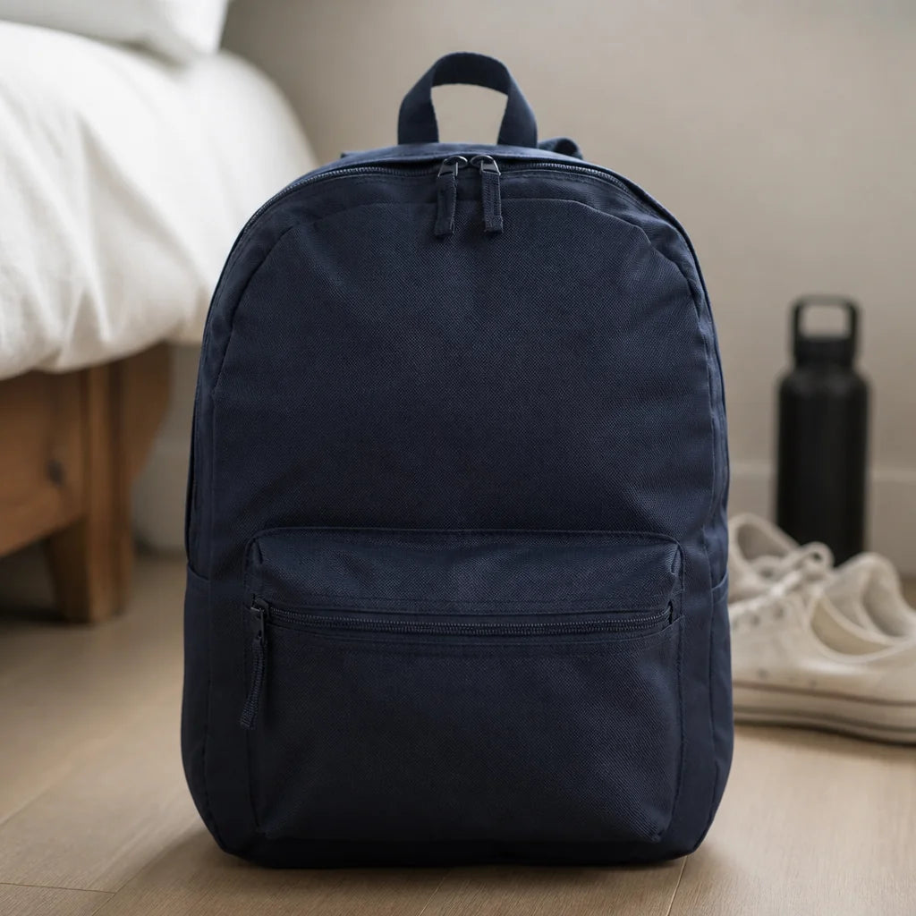 Customizable backpack in navy on a wood floor beside a bed