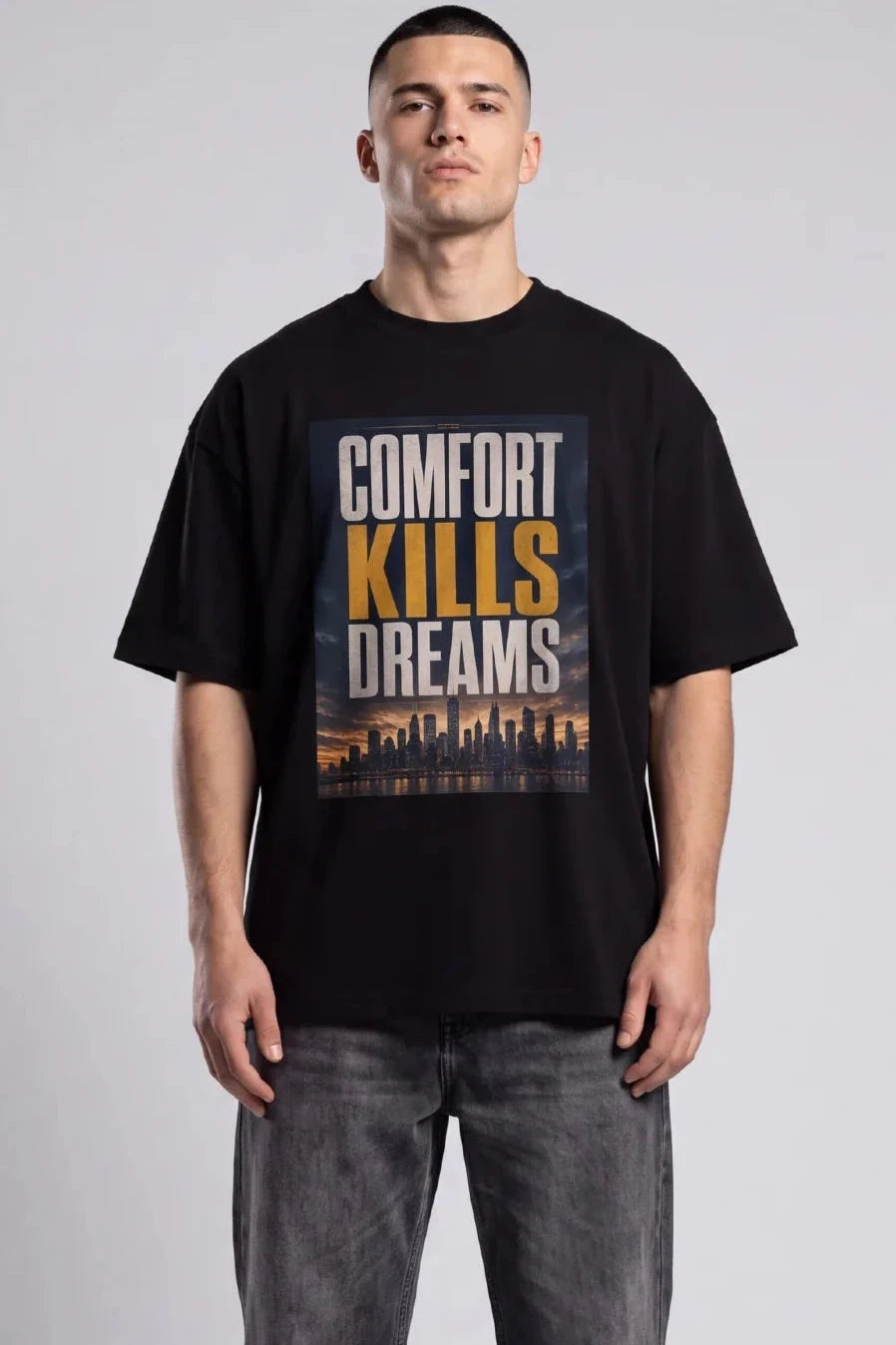 Model wearing a black Comfort Kills Dreams tee with a sunset city skyline print